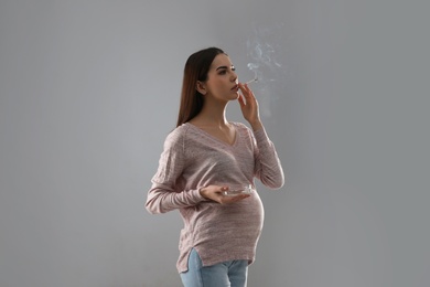 Photo of Young pregnant woman smoking cigarette on grey background