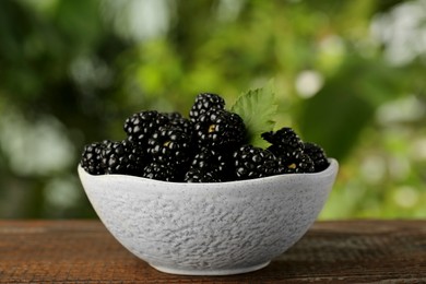 Photo of Bowl of fresh ripe blackberries on wooden table outdoors, closeup