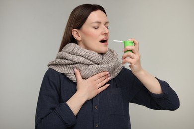 Photo of Woman with scarf using throat spray on grey background