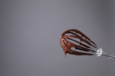 Photo of Chocolate cream flowing from whisk on grey background, space for text