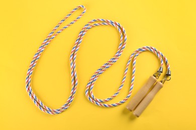 Photo of Skipping rope on yellow background, top view. Sports equipment