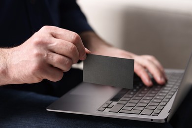 Photo of Man with laptop holding blank business card on blurred background, closeup