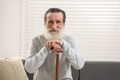 Photo of Senior man with walking cane on sofa indoors