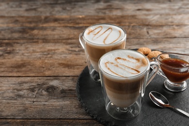 Photo of Glass cups of caramel macchiato served on wooden table, space for text