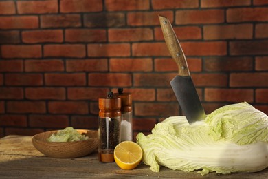 Photo of Fresh Chinese cabbage, knife, spices and lemon on wooden table