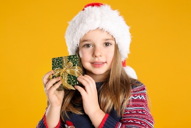 Photo of Cute child in Santa with Christmas gift on yellow background
