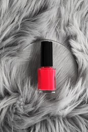 Photo of Bright nail polish in bottle on grey faux fur, top view