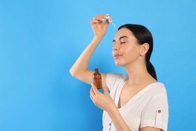 Photo of Young woman applying essential oil onto face on light blue background. Space for text