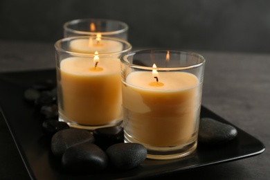 Dark plate with burning candles and rocks on table