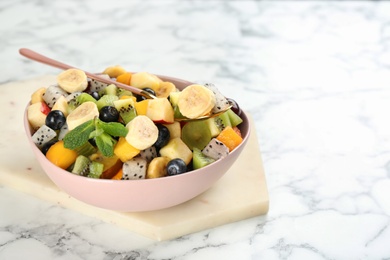 Photo of Delicious exotic fruit salad on white marble table. Space for text