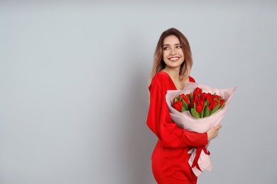 Happy woman with red tulip bouquet on light grey background, space for text. 8th of March celebration