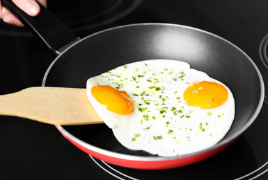 Photo of Woman cooking eggs in frying pan on stove, closeup