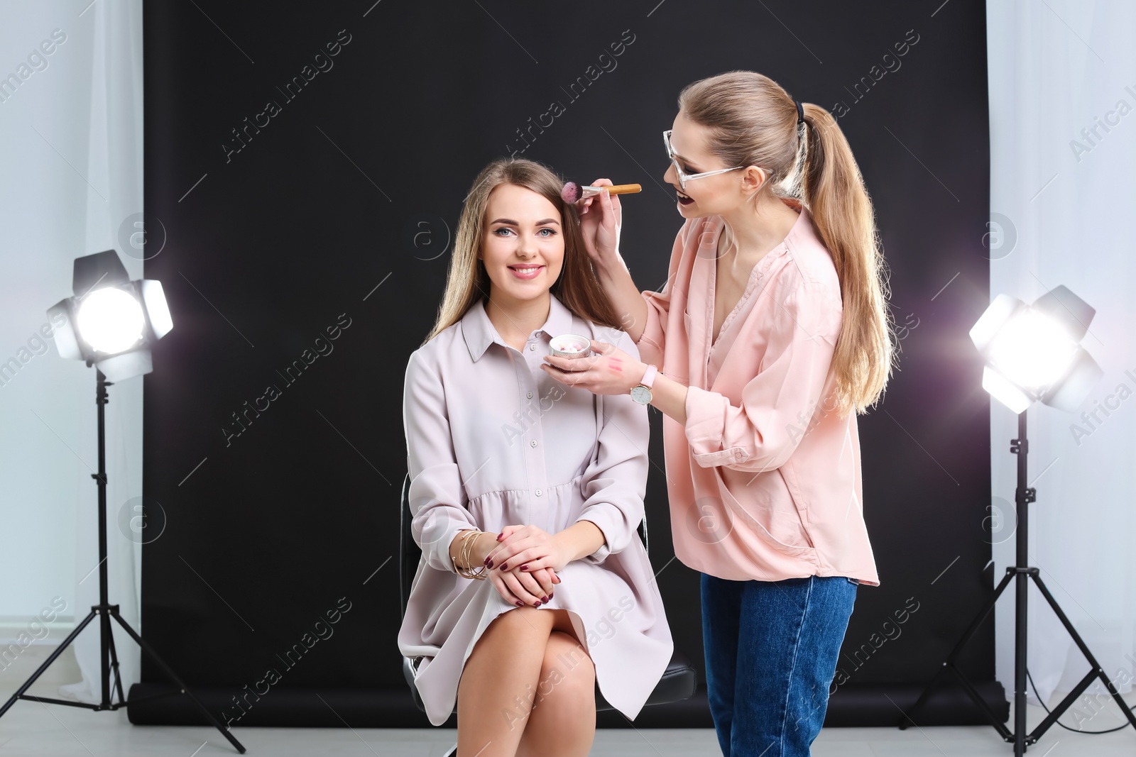 Photo of Professional makeup artist working with beautiful young woman in photo studio