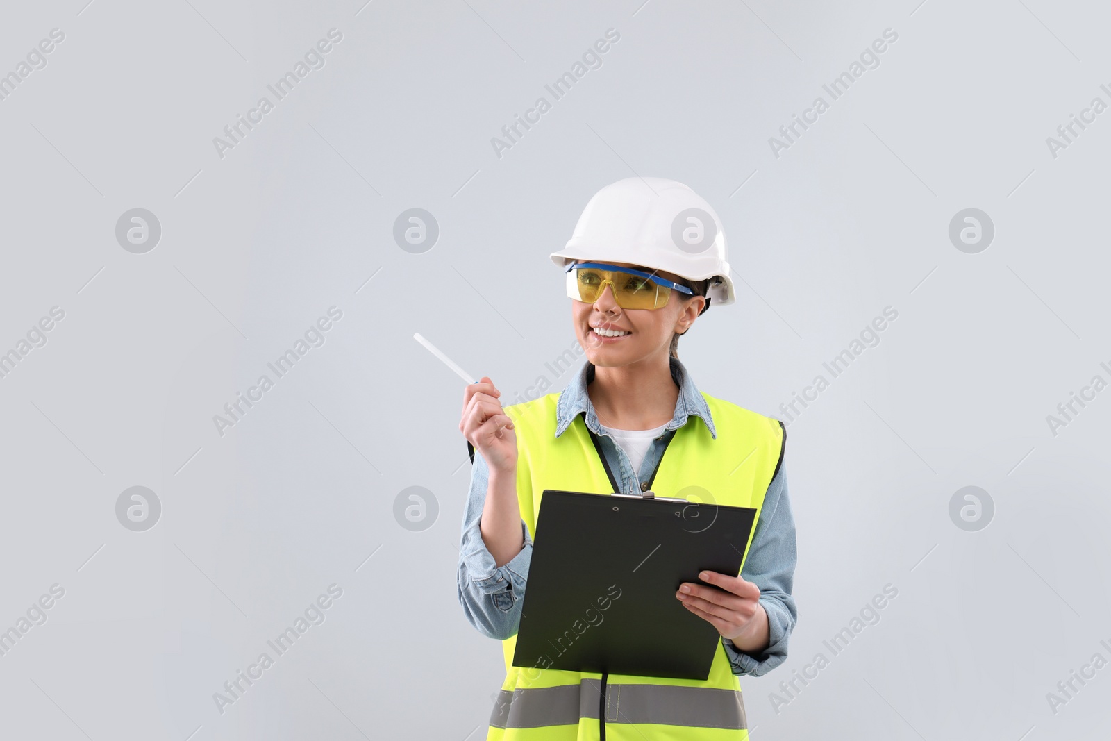 Photo of Female industrial engineer in uniform with clipboard on light background. Safety equipment