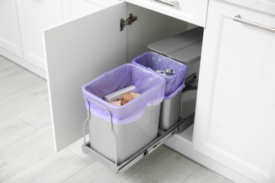 Photo of Open cabinet with full trash bins for separate waste collection in kitchen