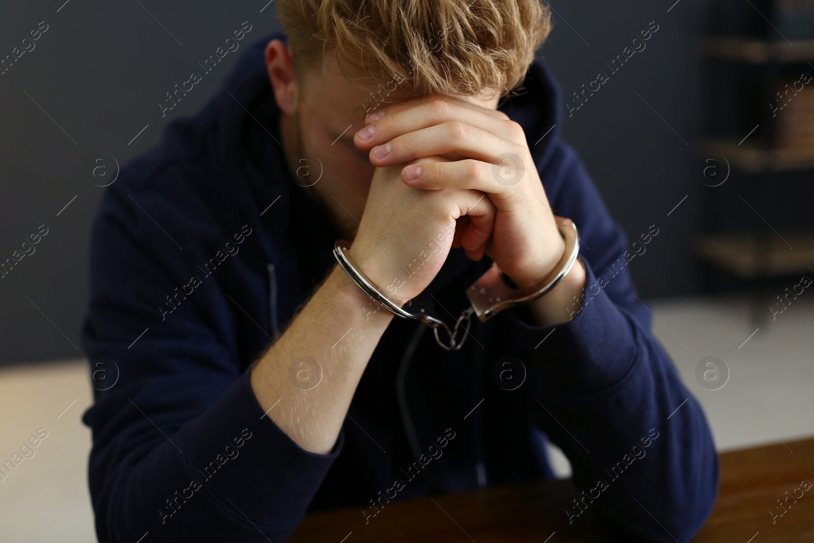 Photo of Man detained in handcuffs at desk indoors. Criminal law