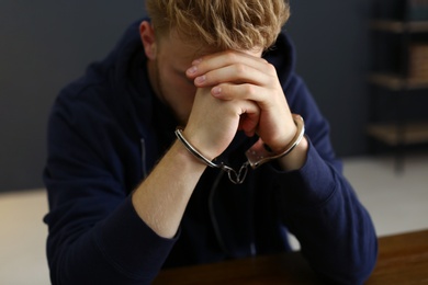 Man detained in handcuffs at desk indoors. Criminal law