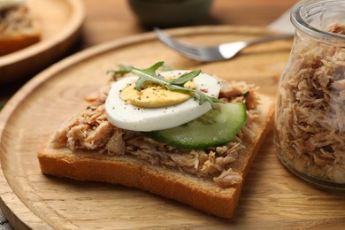 Photo of Delicious sandwich with tuna, greens, cucumber, boiled egg and spices on wooden board, closeup