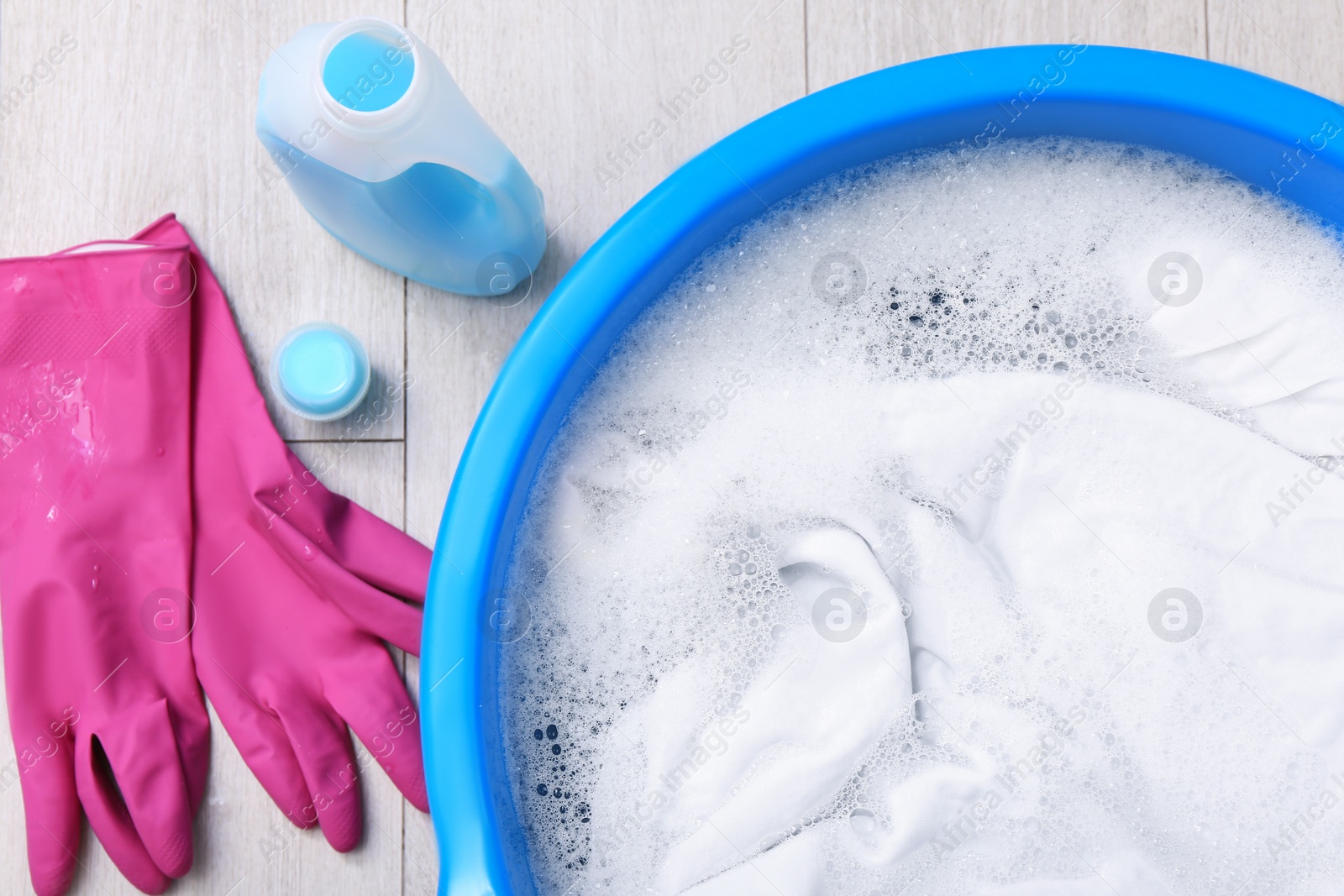 Photo of Basin with white garment near detergent and gloves on floor, flat lay. Hand washing laundry