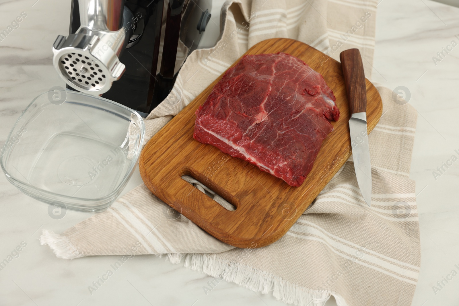 Photo of Electric meat grinder with beef on white marble table, above view