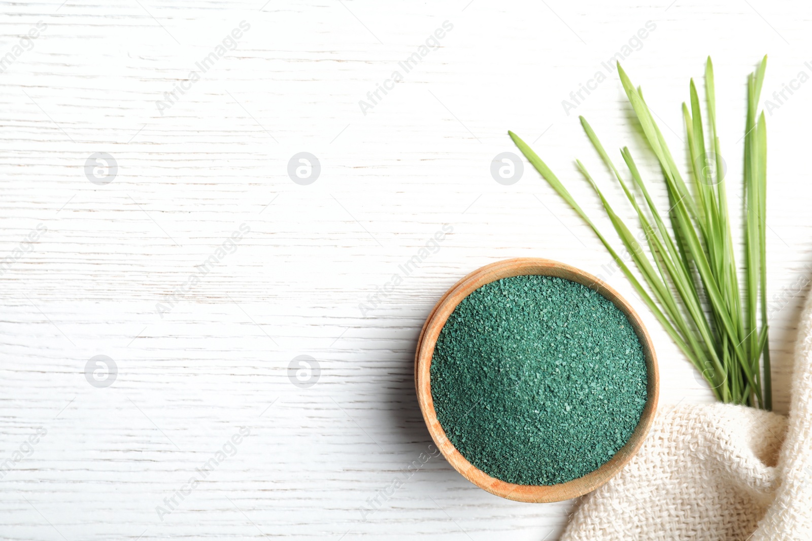 Photo of Bowl of spirulina powder, grass and napkin on white background, flat lay. Space for text