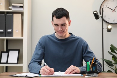 Photo of Man taking notes at wooden table in office