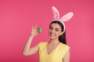 Beautiful woman in bunny ears headband holding Easter egg on color background