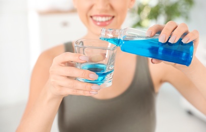 Photo of Woman pouring mouthwash from bottle into glass, closeup. Teeth care
