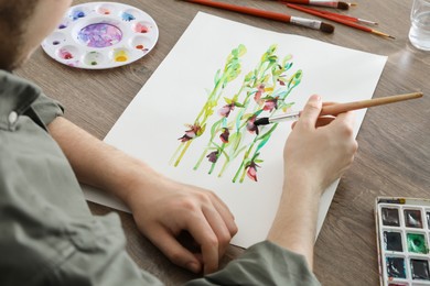 Man painting flowers with watercolor at wooden table, closeup. Creative artwork