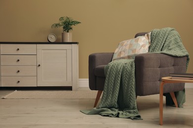 Living room interior with comfortable grey armchair, pillow and plaid