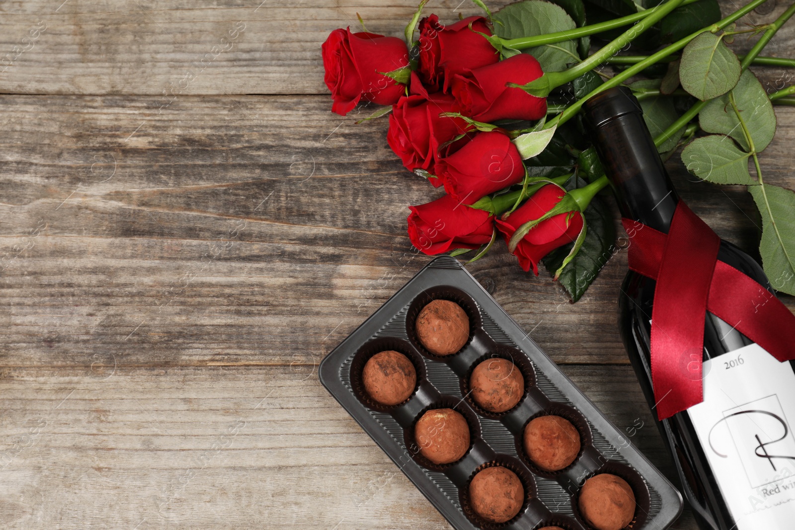 Photo of Bottle of red wine, chocolate truffles and roses on wooden table, flat lay. Space for text