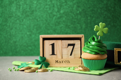 Decorated cupcake, wooden block calendar, hat and coins on grey table. St. Patrick's Day celebration