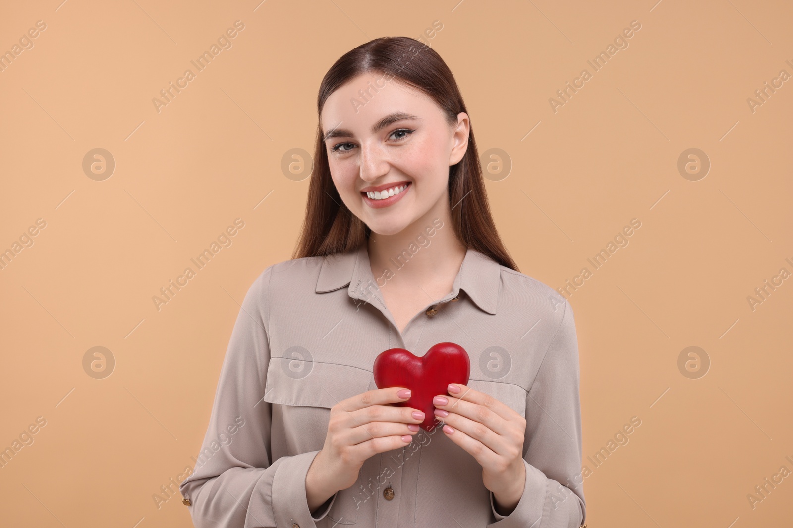 Photo of Smiling woman holding red heart on beige background