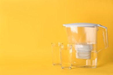 Photo of Filter jug and glasses with purified water on yellow background. Space for text