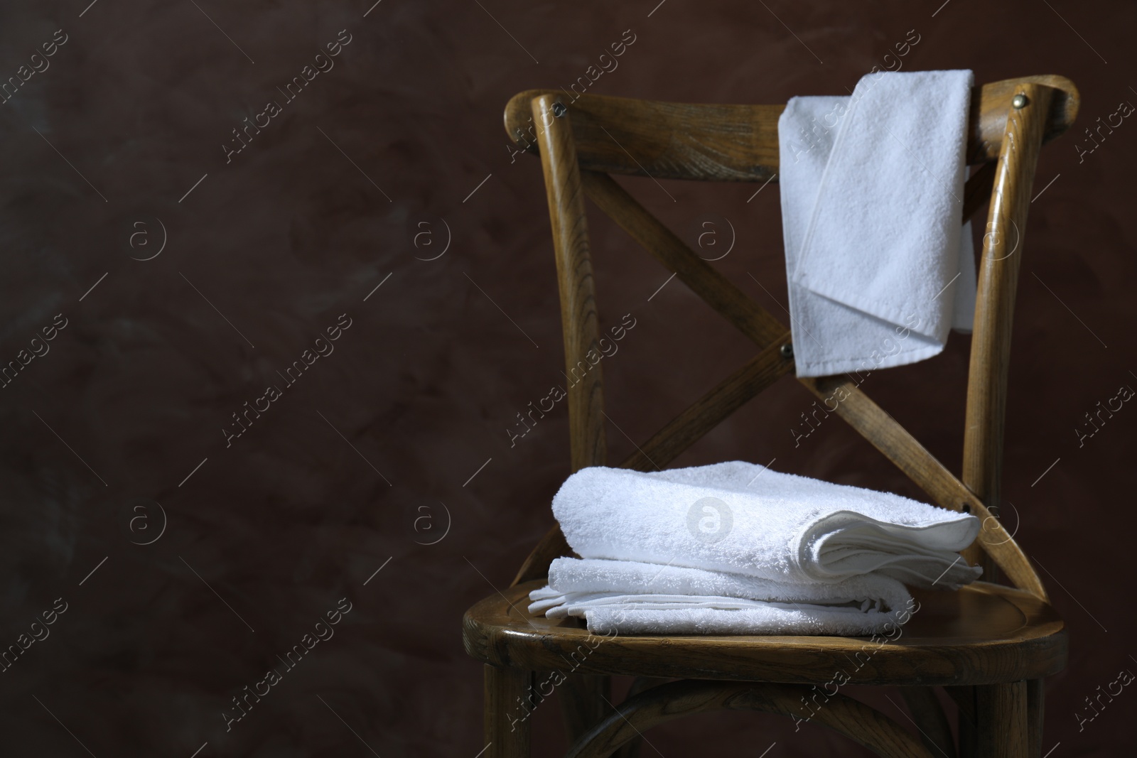 Photo of White terry towels on wooden chair against brown background. Space for text