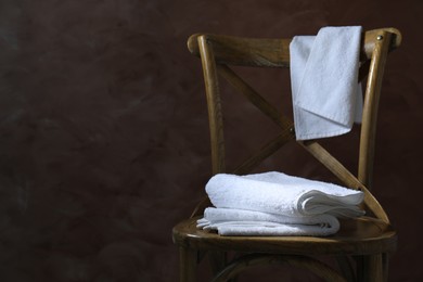 Photo of White terry towels on wooden chair against brown background. Space for text