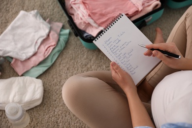 Photo of Pregnant woman writing packing list for maternity hospital at home, above view
