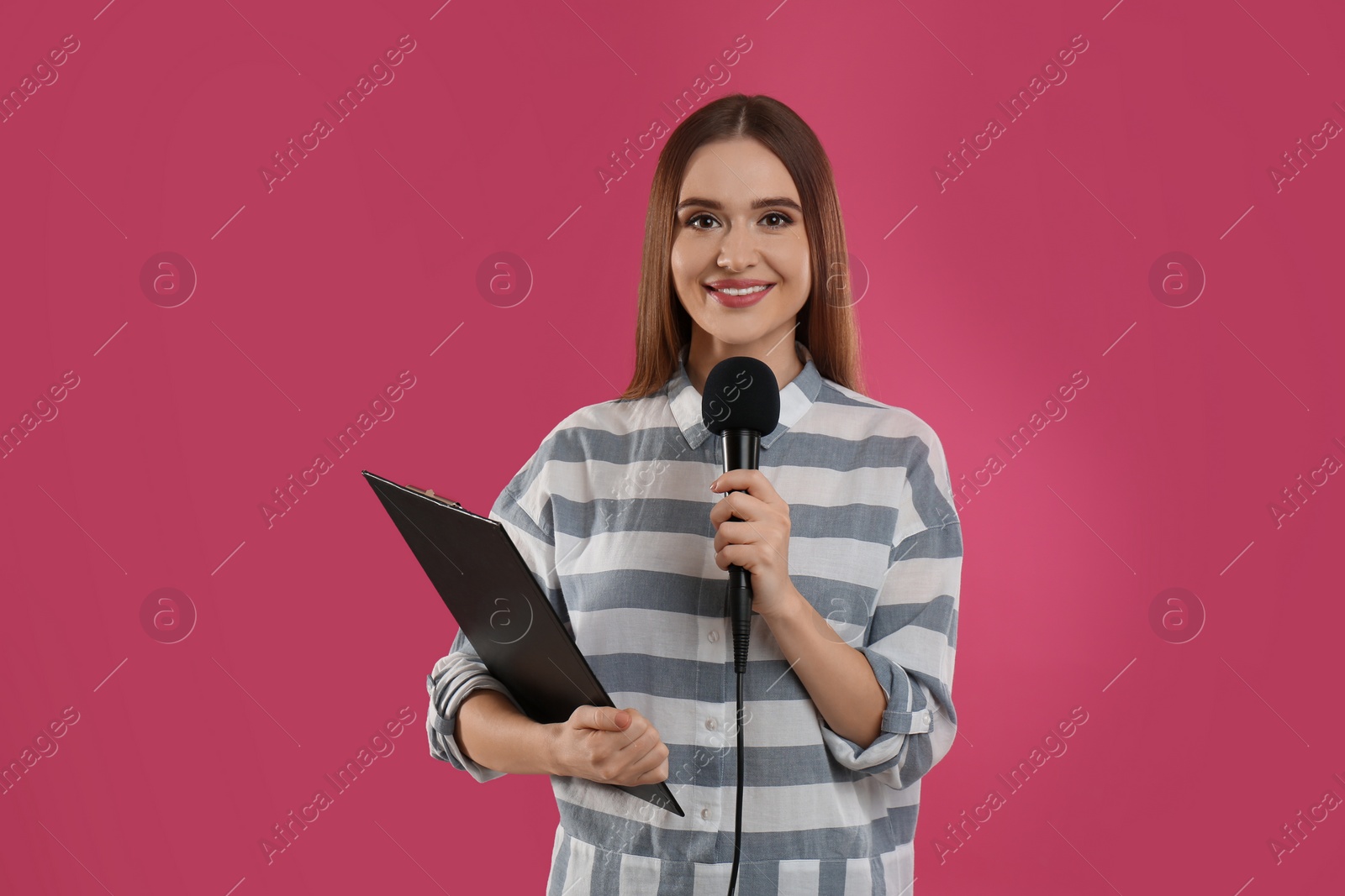 Photo of Young female journalist with microphone and clipboard on pink background