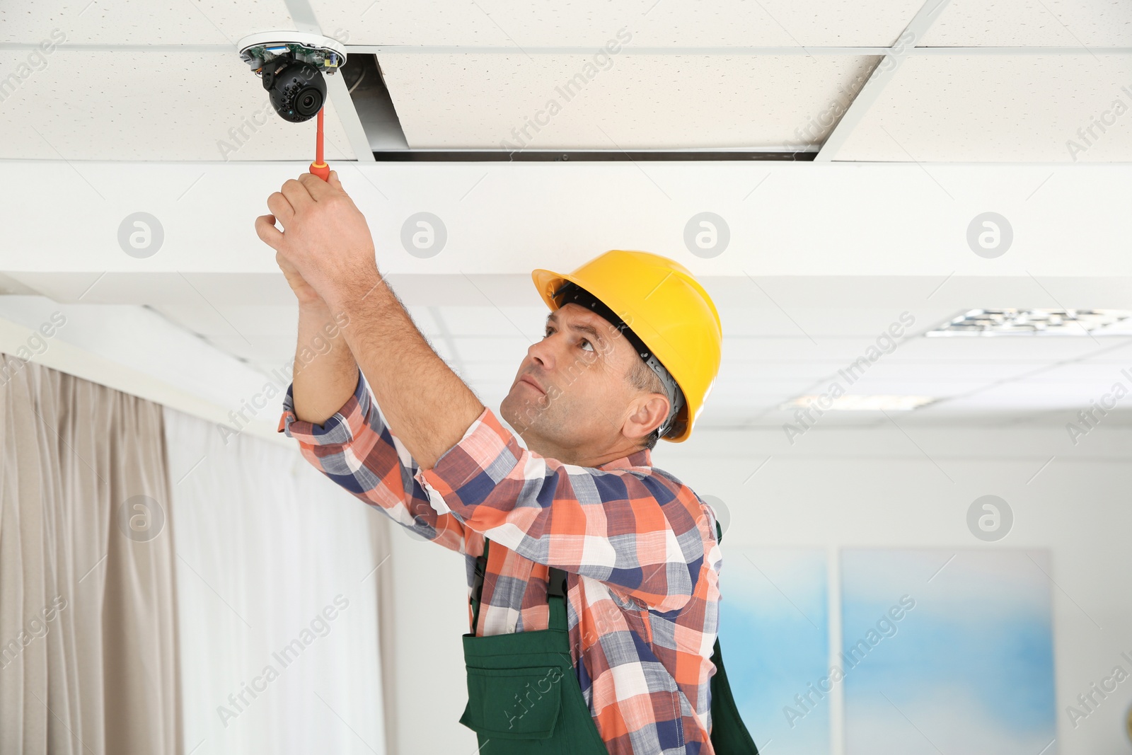 Photo of Electrician with screwdriver repairing CCTV camera indoors