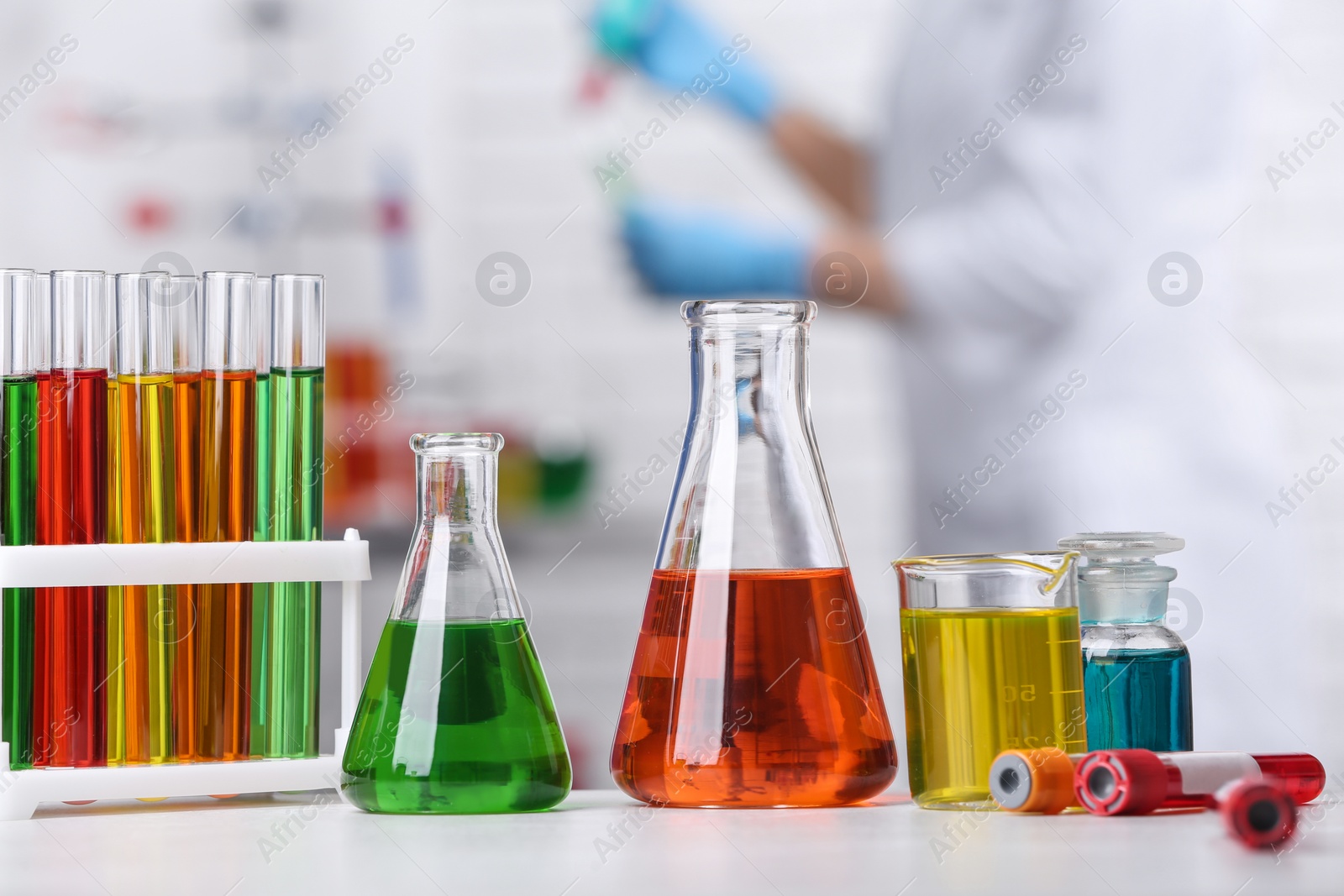 Photo of Different glassware on table and scientist in chemistry laboratory