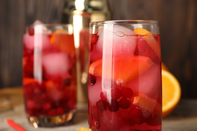 Tasty cranberry cocktail with ice cubes and orange in glasses on table, closeup