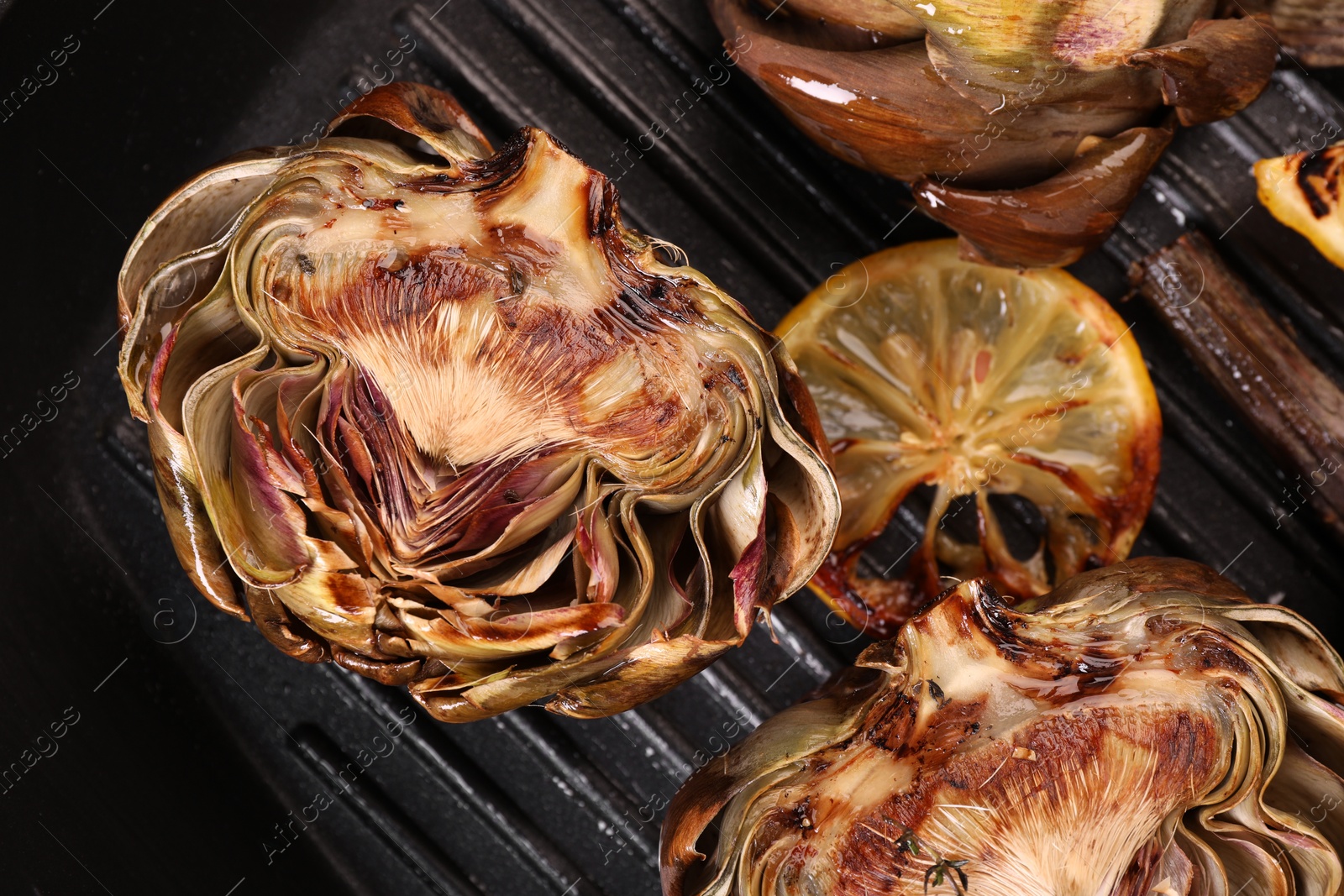 Photo of Tasty grilled artichokes and lemon slice on pan, top view