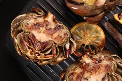 Photo of Tasty grilled artichokes and lemon slice on pan, top view