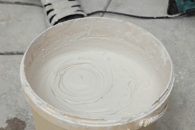 Photo of Bucket with plaster on concrete floor indoors, closeup