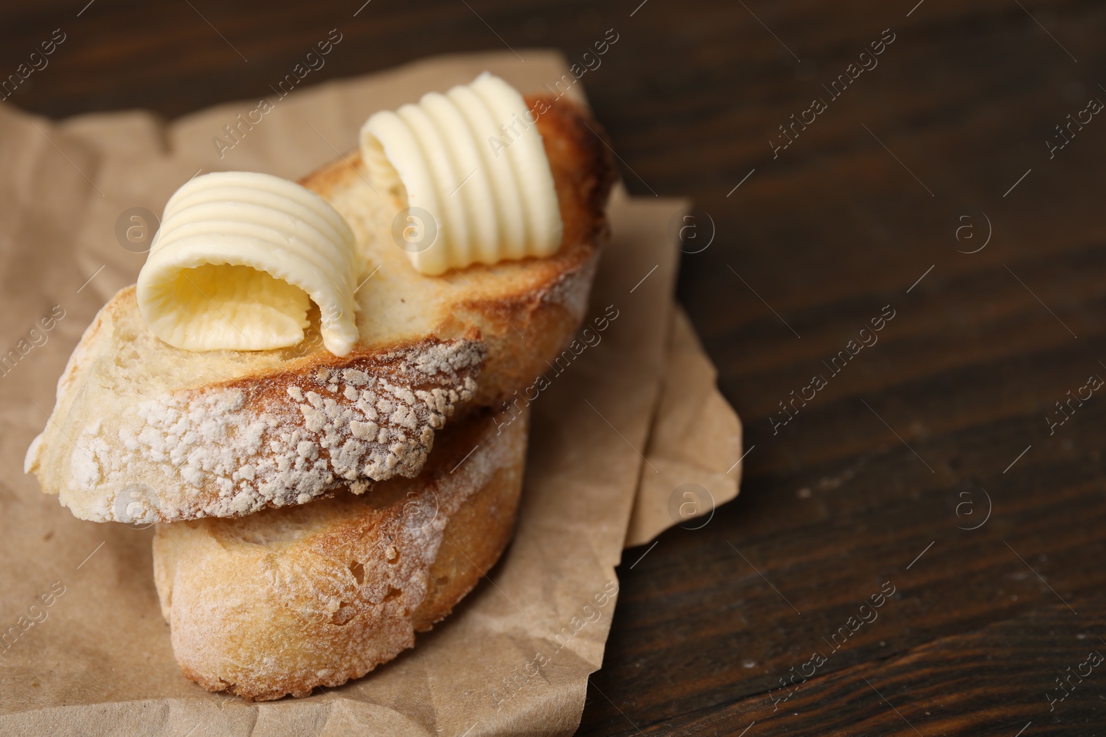 Photo of Tasty butter curls and slices of bread on wooden table, closeup. Space for text