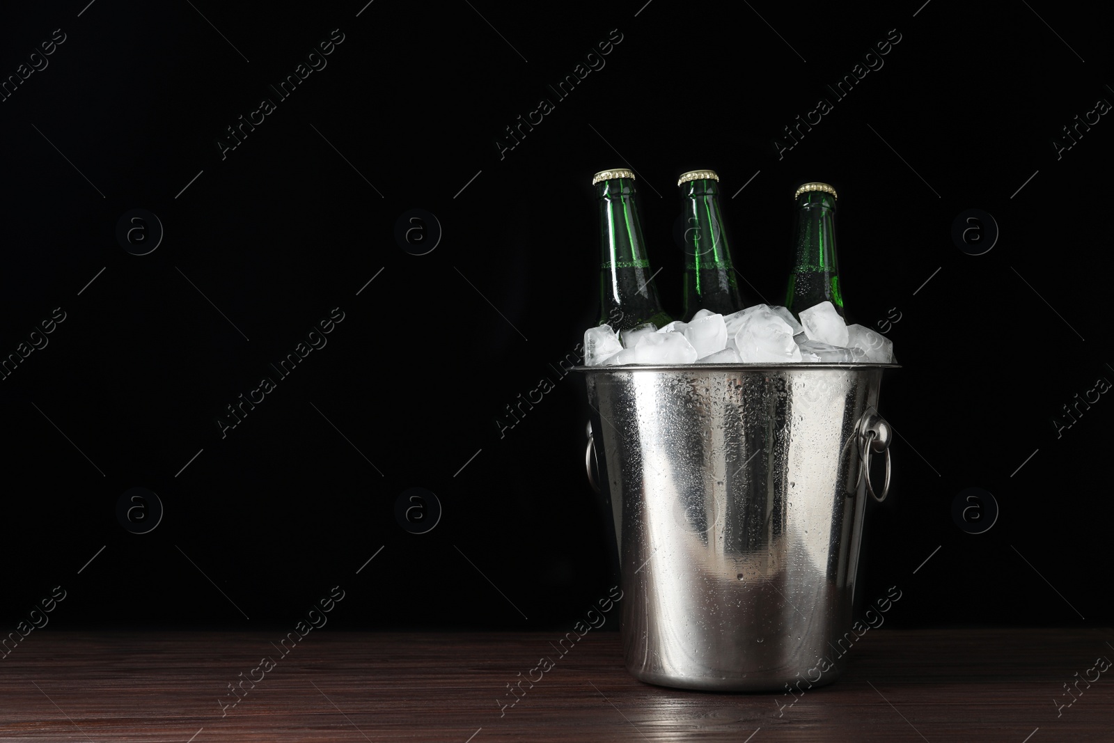 Photo of Metal bucket with bottles of beer and ice cubes on wooden table. Space for text