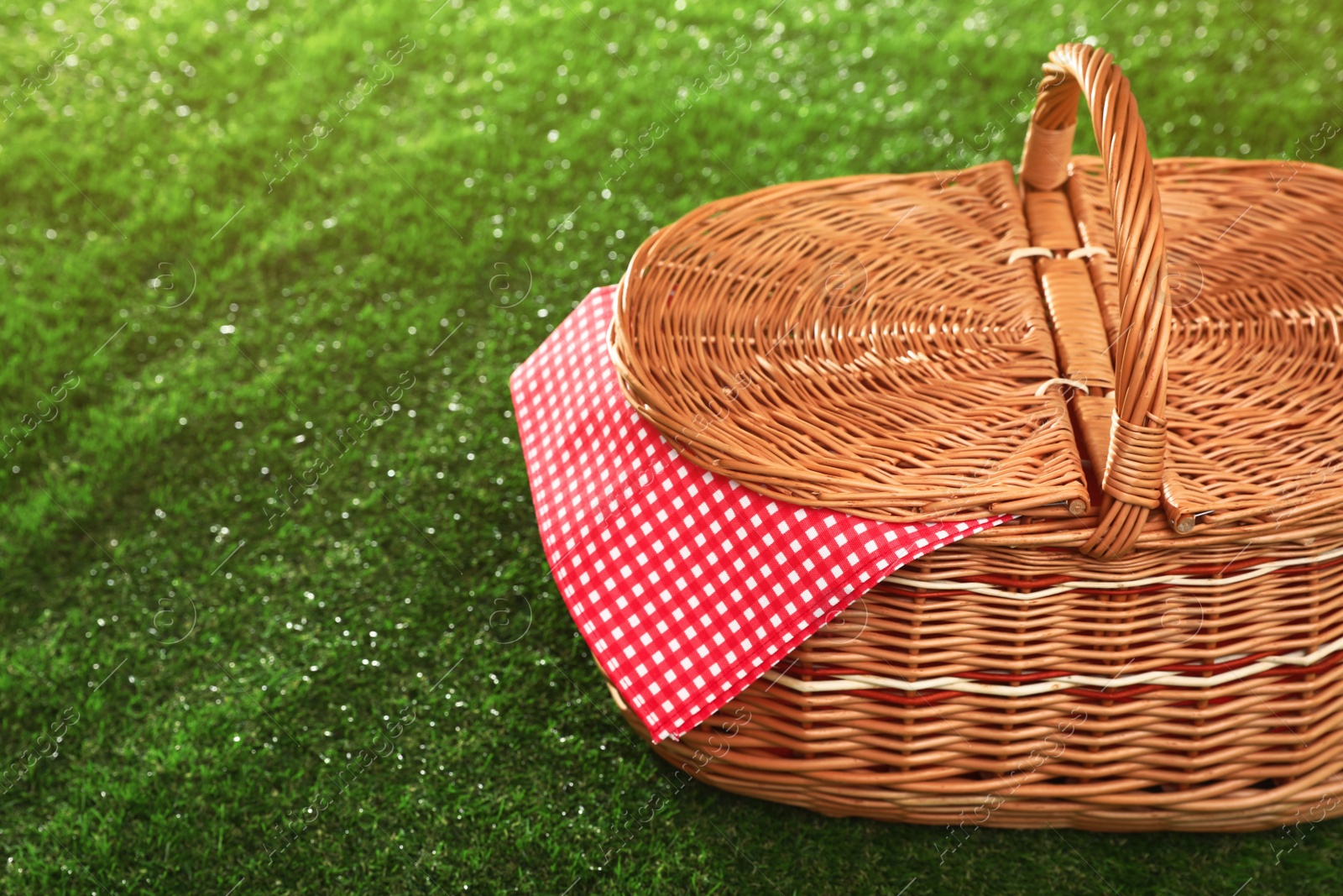 Photo of Closed picnic basket with napkin on grass, space for text