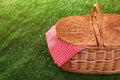 Closed picnic basket with napkin on grass, space for text