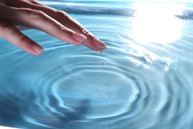 Woman touching clear water, closeup. Making ripples