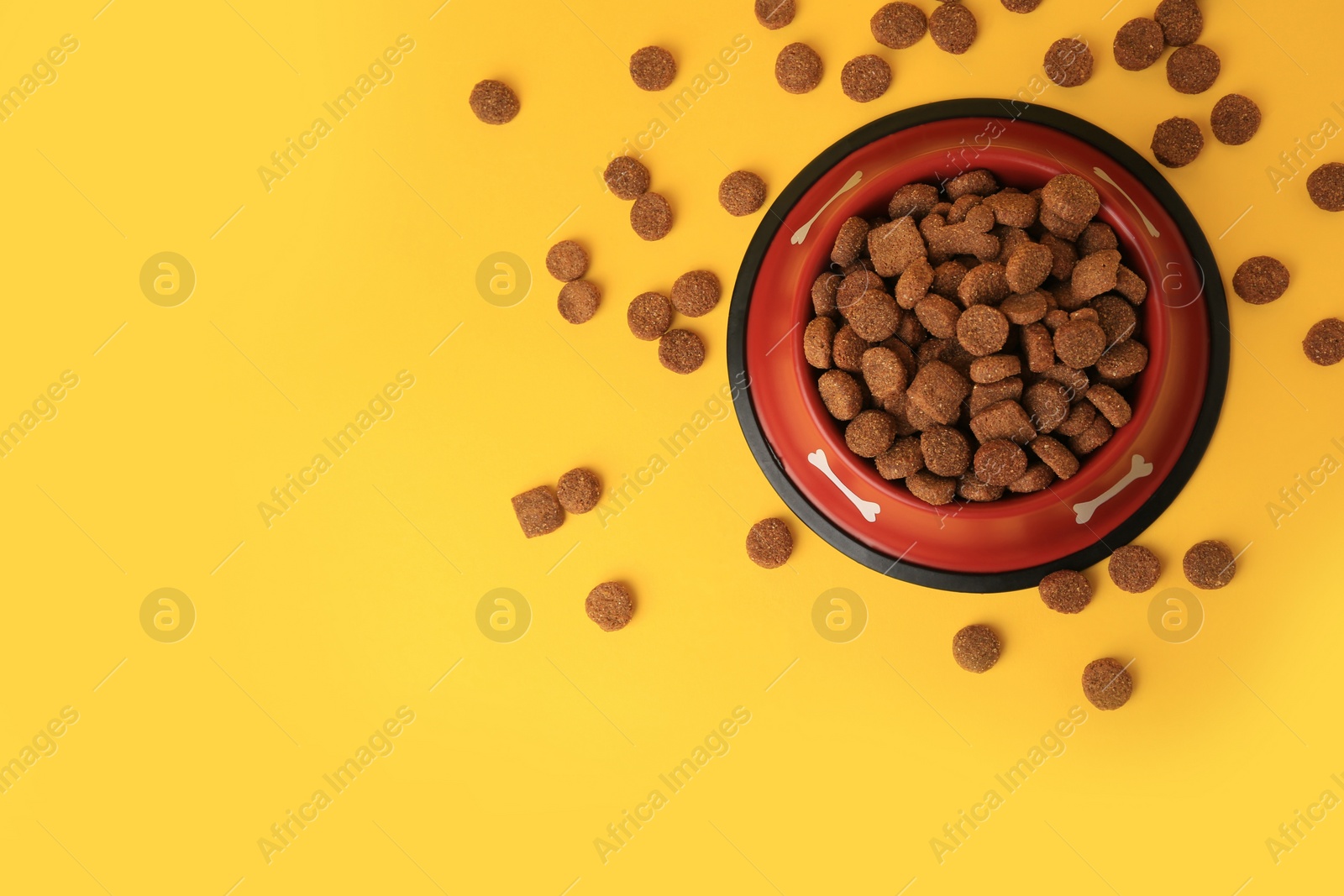 Photo of Dry dog food and feeding bowl on orange background, flat lay. Space for text